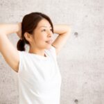 両手を頭の後ろに組んで胸を開く女性
