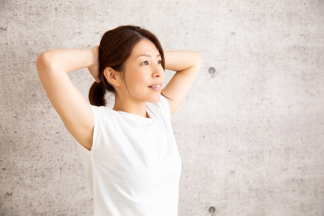 両手を頭の後ろに組んで胸を開く女性