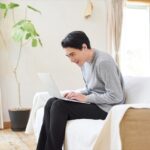 窓辺でノートパソコンに向かう男性