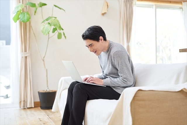 窓辺でノートパソコンに向かう男性